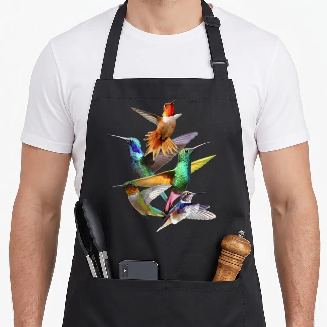 Flight hummingbird lover apron - Four hummingbirds in flight with green blue orange and brown feathers overlapping — shown on a black cotton canvas apron against a white background
