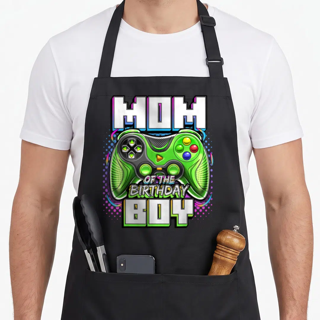 Birthday party video game apron - Green game controller with MOM OF THE BIRTHDAY BOY text and colorful dots — shown on a black cotton canvas apron against a white background