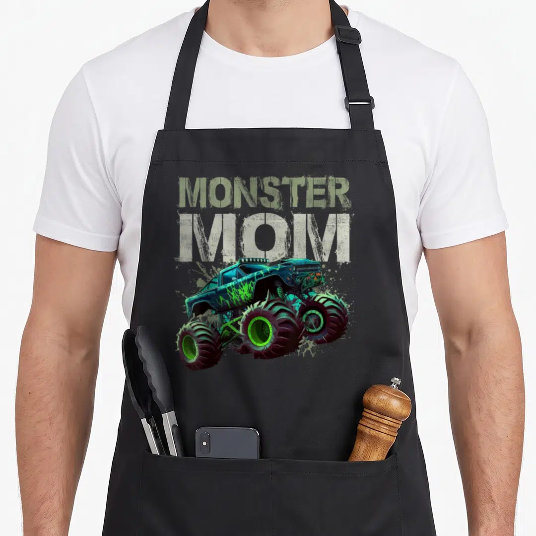 Funny family truck apron - MONSTER MOM text above a blue green cartoon monster truck illustration — shown on a black cotton canvas apron against a white background