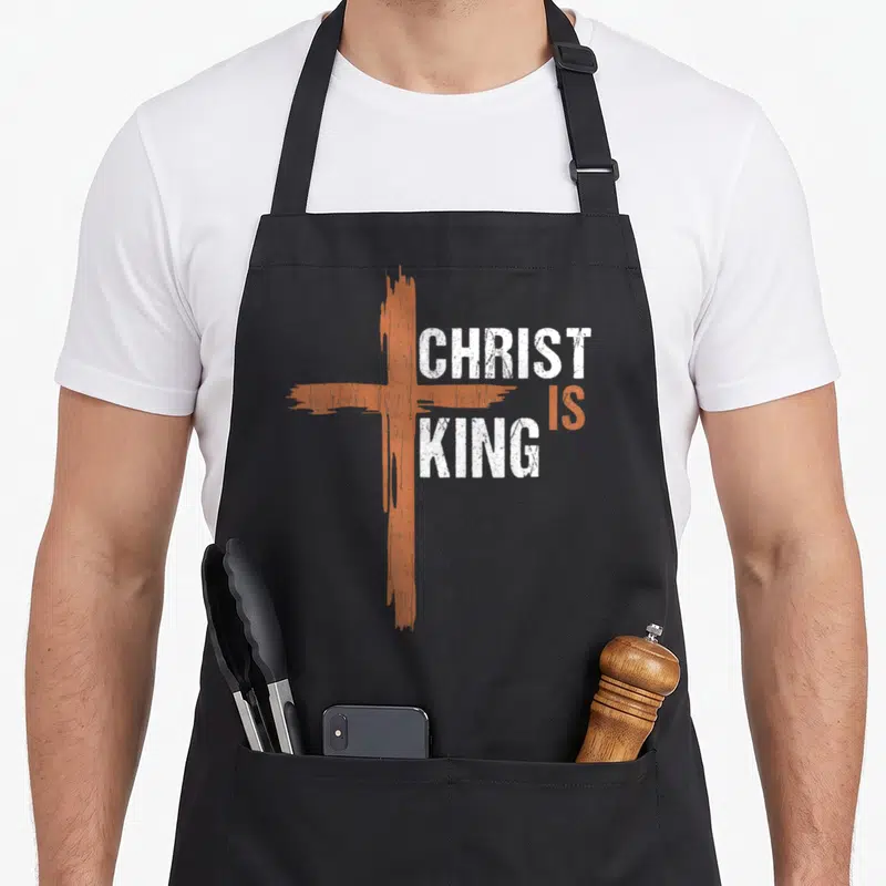 Christ christian king of the grill apron - Orange distressed cross with white CHRIST IS KING text — shown on a black cotton canvas apron against a white background