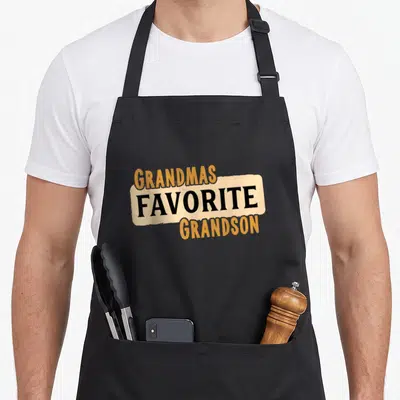 Grandson grandma's aprons - Stacked text GRANDMAS FAVORITE GRANDSON in orange black and beige banner — shown on a black cotton canvas apron against a white background