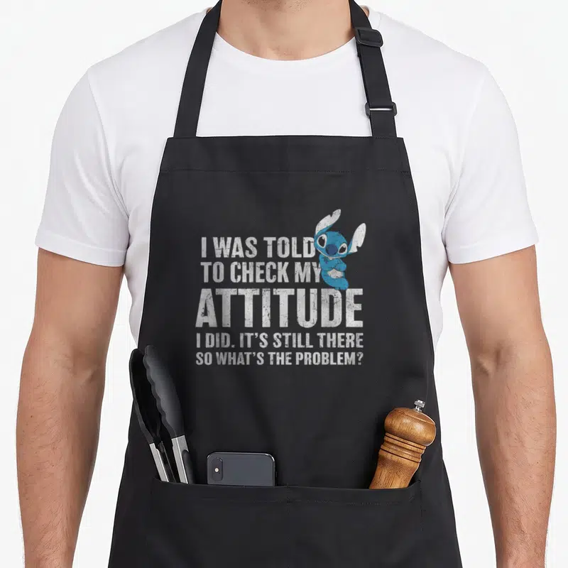 Problem attitude aprons - Stitch character and sarcastic quote about attitude in distressed white and blue text — shown on a black cotton canvas apron against a white background