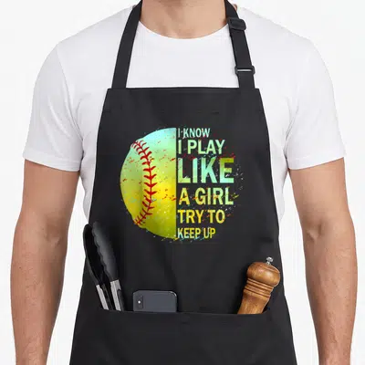 Funny softball apron - Distressed yellow softball with red stitching next to stacked green and white text reading I — shown on a black cotton canvas apron against a white background