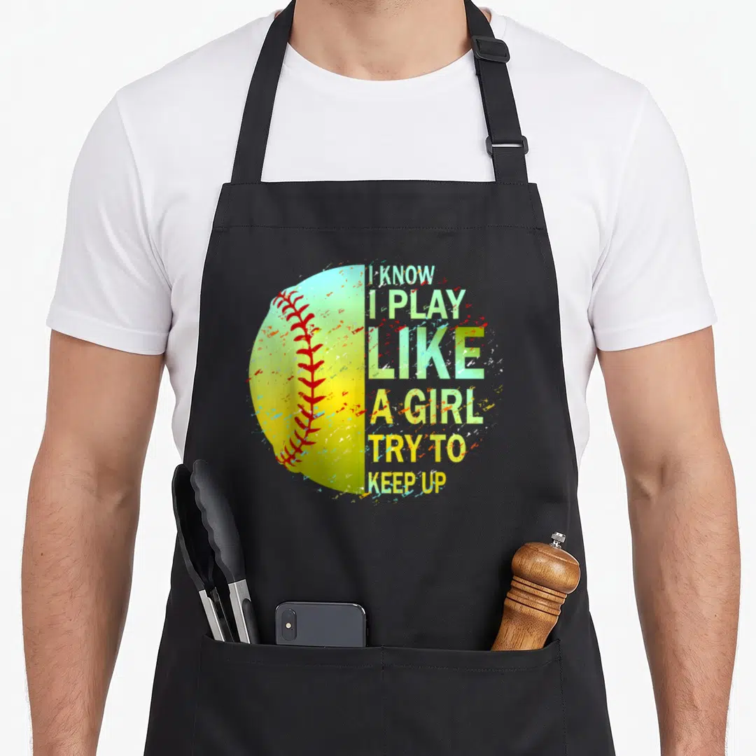 Funny softball apron - Distressed yellow softball with red stitching next to stacked green and white text reading I — shown on a black cotton canvas apron against a white background