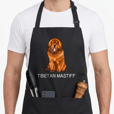 Tibetan cooking with dog apron - Cartoon brown and white Tibetan Mastiff sitting above white TIBETAN MASTIFF text — shown on a black cotton canvas apron against a white background