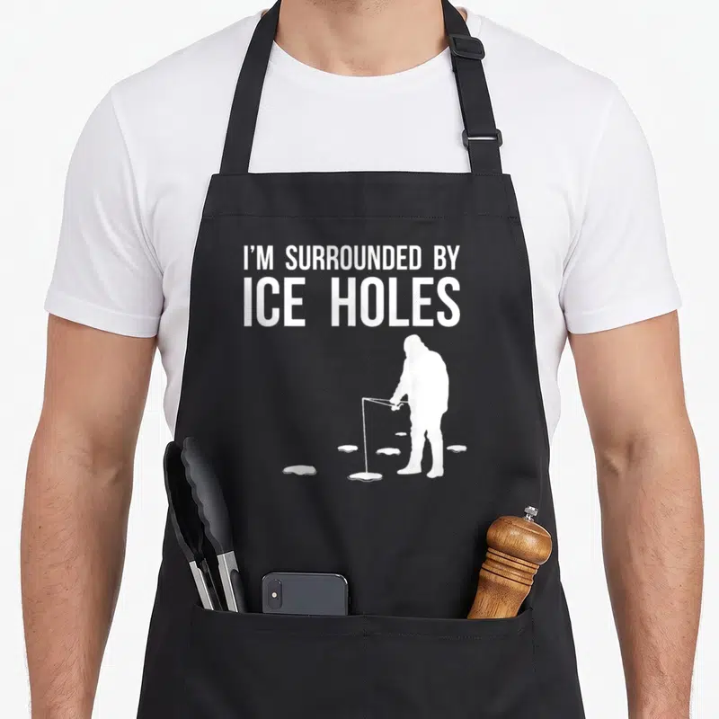 Ice fishing aprons - White text I'M SURROUNDED BY ICE HOLES above fisherman silhouette and oval holes on black — shown on a black cotton canvas apron against a white background