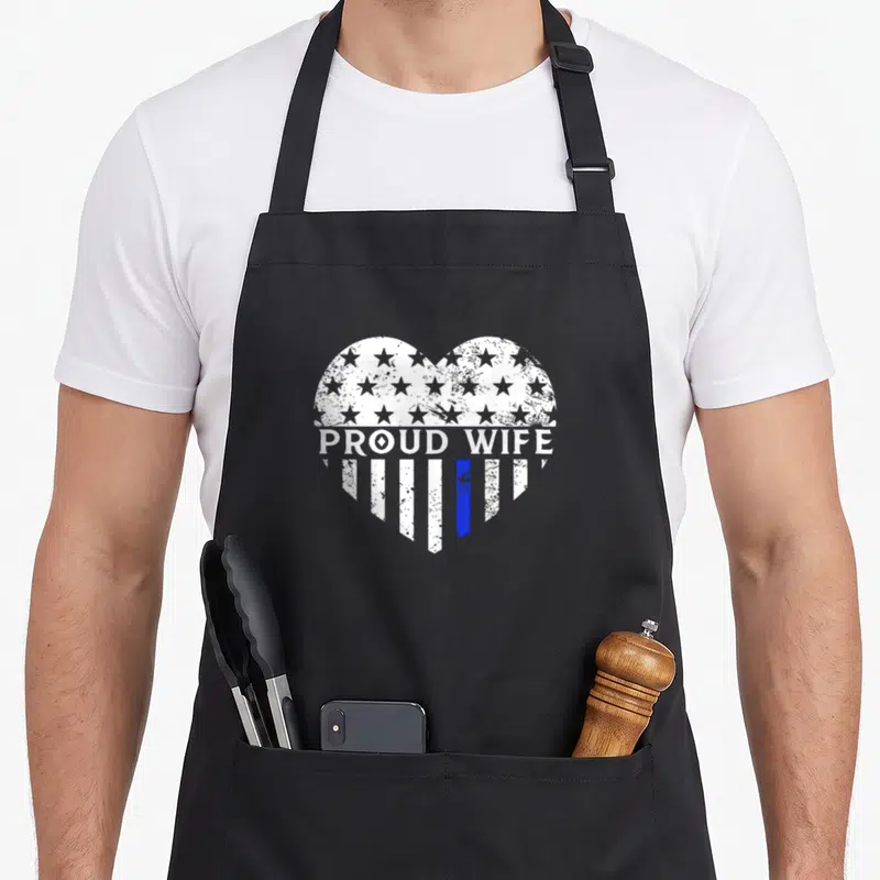 Flag wife apron - Distressed heart with white stars and one blue stripe, PROUD WIFE text across middle — shown on a black cotton canvas apron against a white background