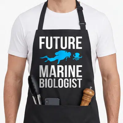 Biologist student aprons - White Future Marine Biologist text framing a blue scuba diver and octopus silhouette — shown on a black cotton canvas apron against a white background