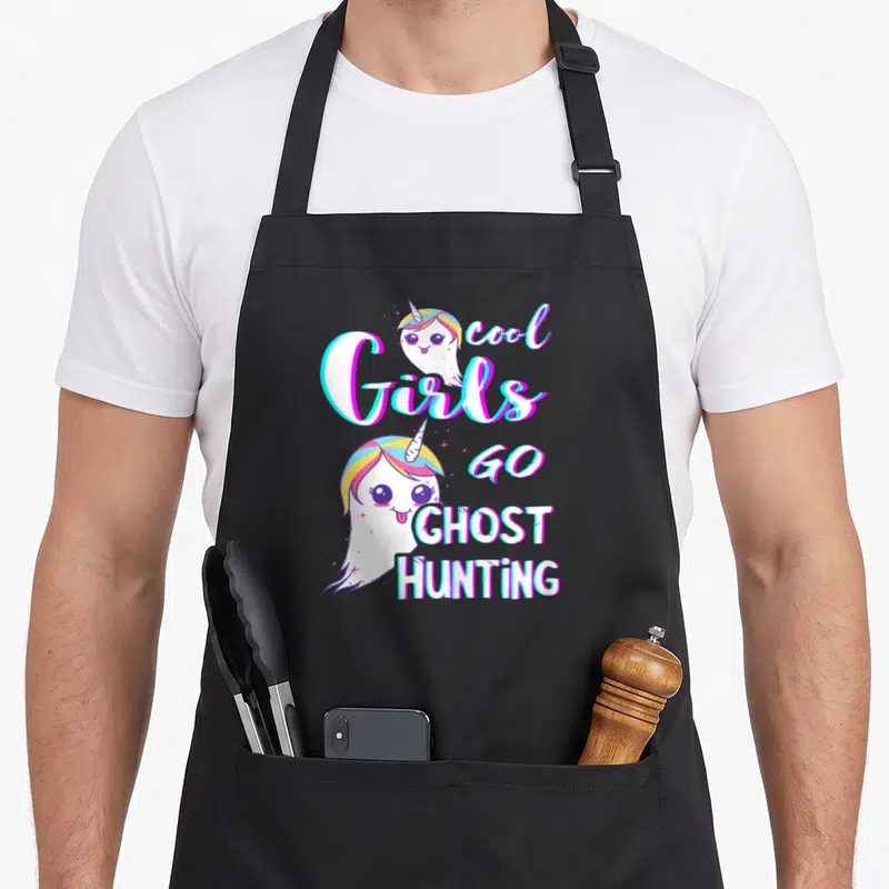 Investigator ghost apron - Cartoon unicorn-ghosts surround Cool Girls Go Ghost Hunting text in white, pink, blue — shown on a black cotton canvas apron against a white background
