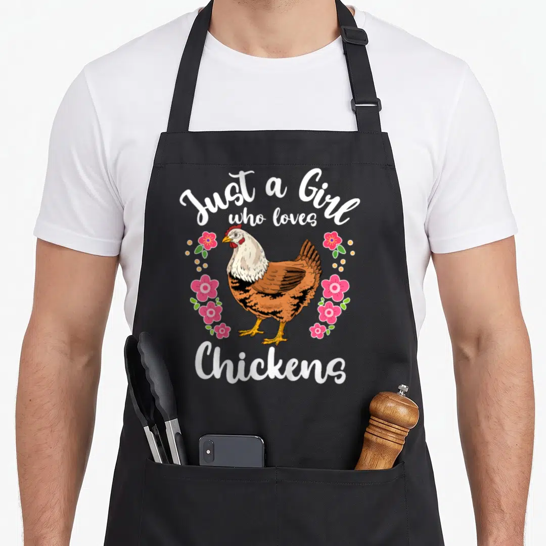 Cute chicken apron - Realistic brown hen surrounded by pink flowers and green leaves with white script text — shown on a black cotton canvas apron against a white background
