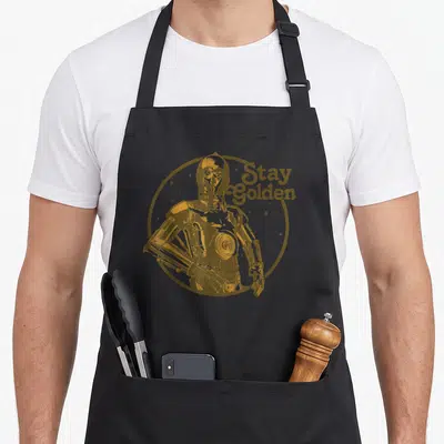 Funny 3po golden apron - Retro gold C-3PO robot inside a circle with Stay Golden text and scattered stars — shown on a black cotton canvas apron against a white background
