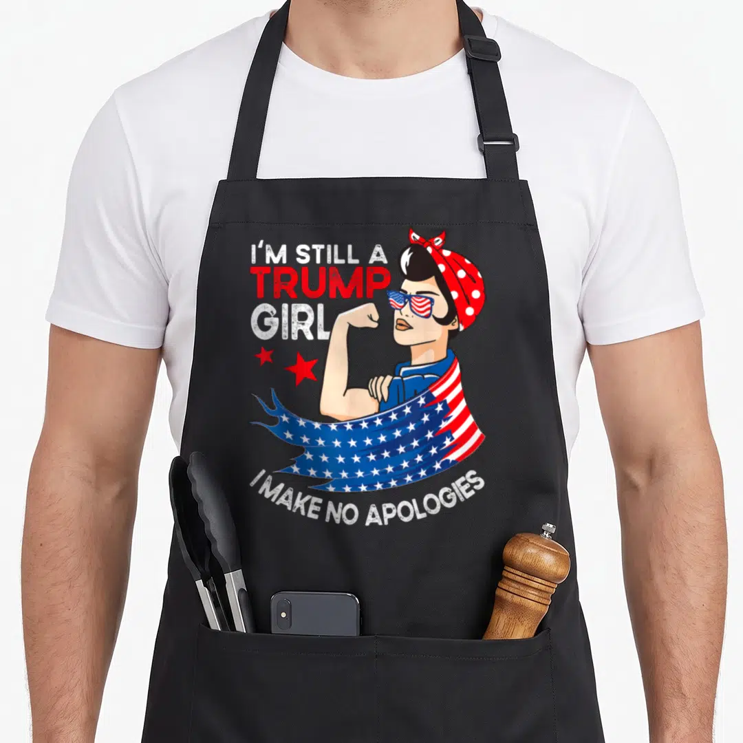 Apology headband apron - Cartoon woman flexing arm with I'M STILL A TRUMP GIRL I MAKE NO APOLOGIES text and three red — shown on a black cotton canvas apron against a white background