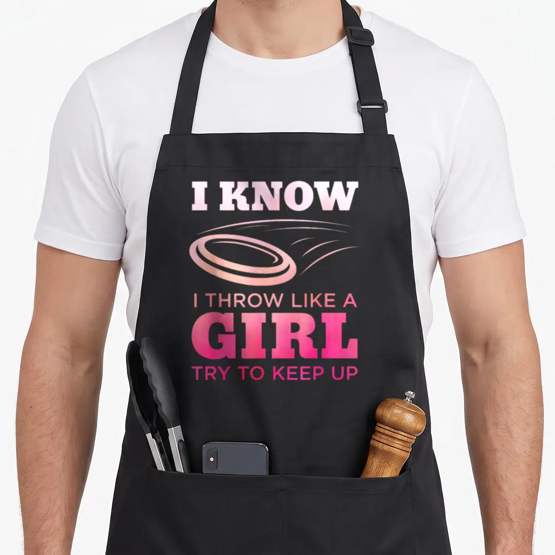 Disc golfing golf apron - Pink typography reading I know I throw like a girl with a flying disc graphic — shown on a black cotton canvas apron against a white background