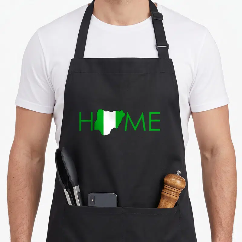 Map nigerian apron - HOME text with Nigeria map flag replacing the O in green and white — shown on a black cotton canvas apron against a white background