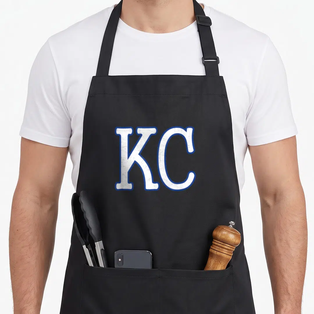 Fan kansas apron - White KC letters with blue outline in a single line of typography — shown on a black cotton canvas apron against a white background