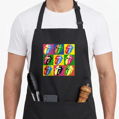 Multi rolling stones apron - 3x3 grid of colorful tongue logos in red blue yellow green pink orange pop art style — shown on a black cotton canvas apron against a white background