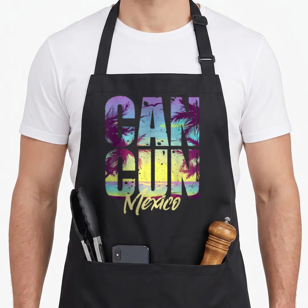 Souvenir mexico apron - Retro CANCUN text filled with beach scene and script Mexico below in purple blue yellow green — shown on a black cotton canvas apron against a white background