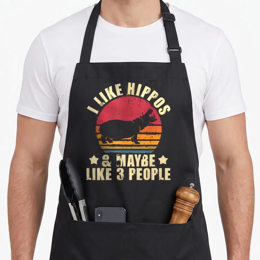 Maybe hippo lover apron - I LIKE HIPPOS text over striped sun with hippo silhouette and two stars — shown on a black cotton canvas apron against a white background