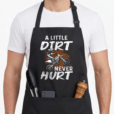 Motorcycle motocross bike apron - Distressed white text A Little Dirt Never Hurt around a motocross rider over a brown — shown on a black cotton canvas apron against a white background