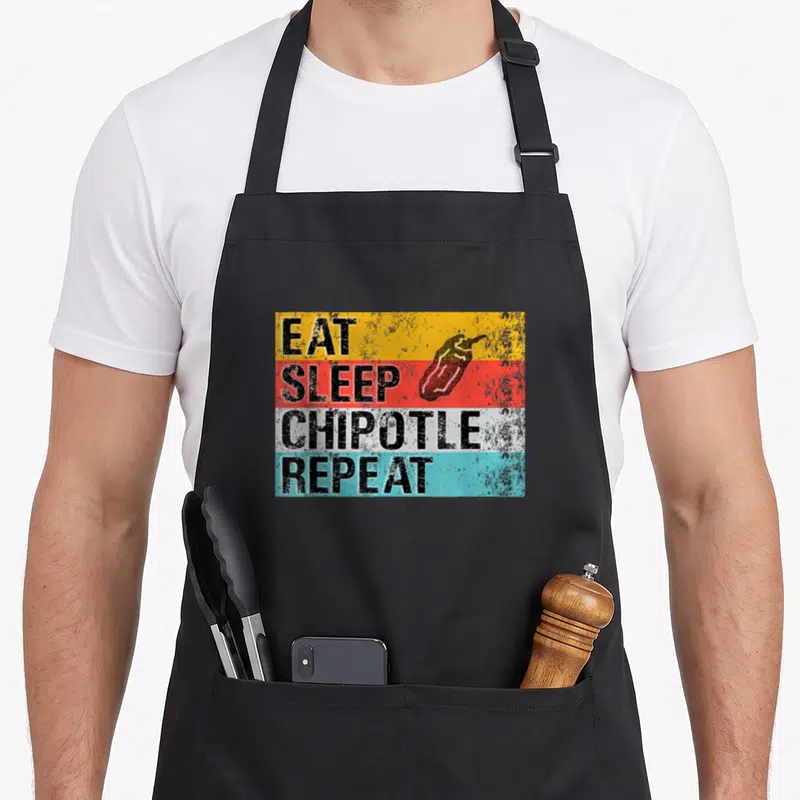 Repeat sleep apron - EAT SLEEP CHIPOTLE REPEAT text on yellow red white and blue stripes with red pepper — shown on a black cotton canvas apron against a white background