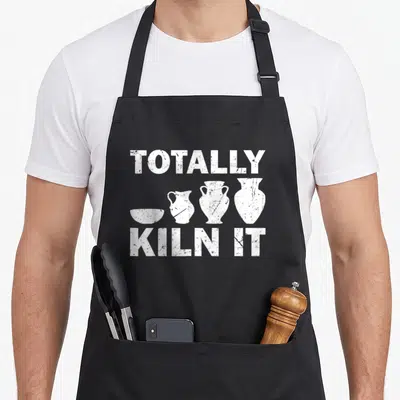 Maker potter apron - White distressed text TOTALLY KILN IT above four pottery vessel silhouettes — shown on a black cotton canvas apron against a white background