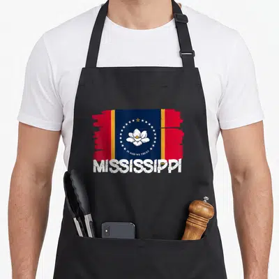 Funny flag mississippi girl apron - Distressed Mississippi state flag with curved IN GOD WE TRUST text and bold — shown on a black cotton canvas apron against a white background