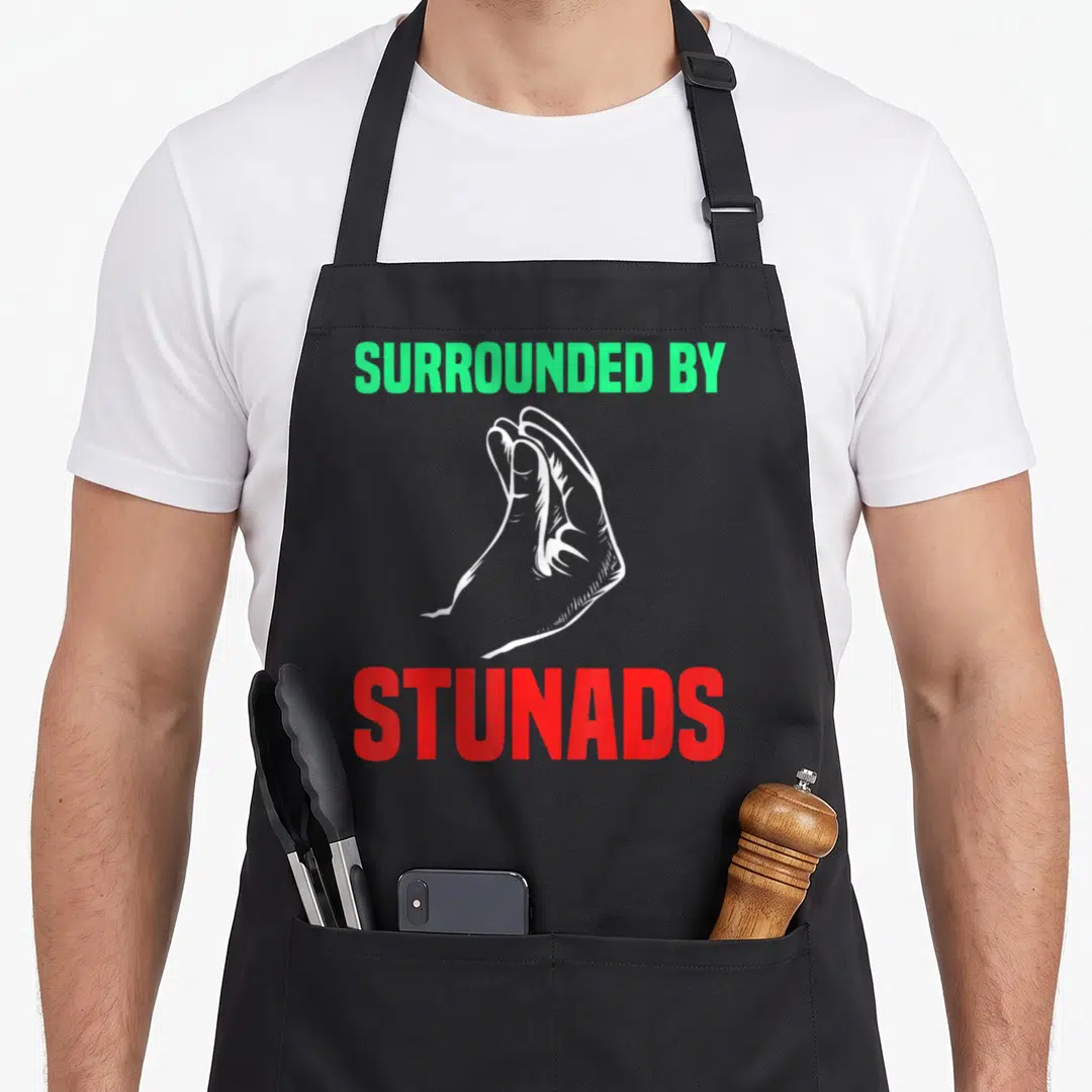 Gesture italy apron - White hand gesture between green Surrounded By and red Stunads text — shown on a black cotton canvas apron against a white background