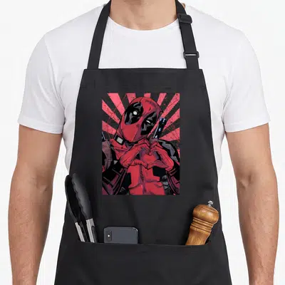 Closed hand apron - Deadpool center making heart shape with hands red black grey sunburst cartoon — shown on a black cotton canvas apron against a white background