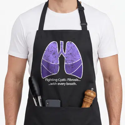 Fight distressed apron - Purple lungs graphic with Fighting Cystic Fibrosis text in distressed style — shown on a black cotton canvas apron against a white background