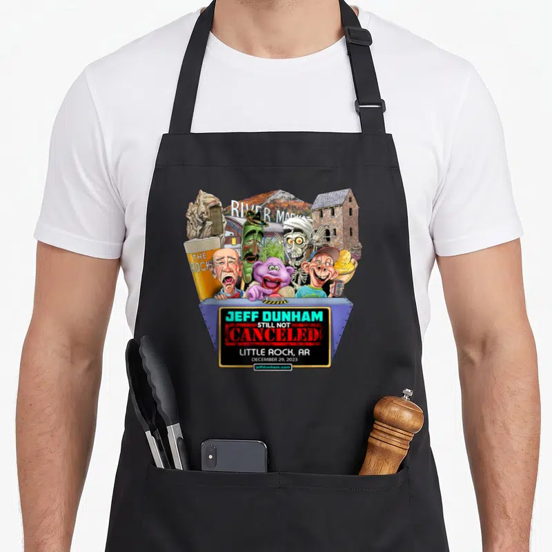 Rock hollywood apron - Jeff Dunham puppets above blue stage with River Market text and Little Rock landmarks — shown on a black cotton canvas apron against a white background