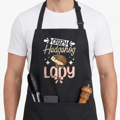 Wild hedgehog lady apron - Cartoon hedgehog between stacked words crazy, Hedgehog, LADY with pink bow and white sparkles — shown on a black cotton canvas apron against a white background