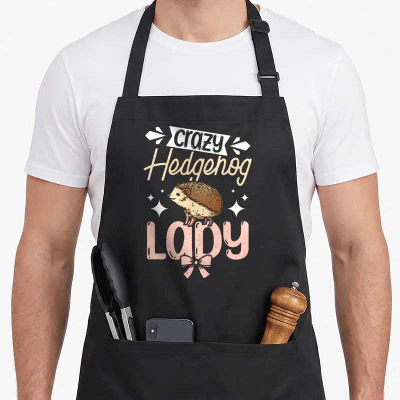 Wild hedgehog lady apron - Cartoon hedgehog between stacked words crazy, Hedgehog, LADY with pink bow and white sparkles — shown on a black cotton canvas apron against a white background
