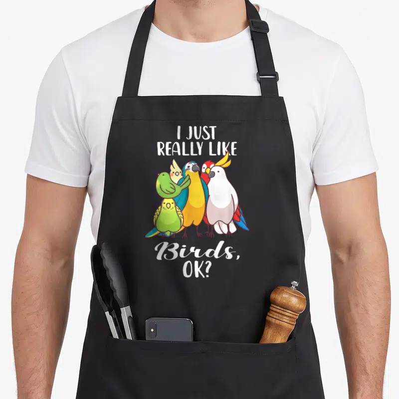 Cockatoo bird apron - I Just Really Like Birds text above colorful parrot cluster — shown on a black cotton canvas apron against a white background