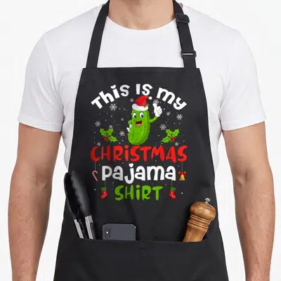 Pickle christmas santa apron - Green pickle in Santa hat giving thumbs up with Christmas text and decorations — shown on a black cotton canvas apron against a white background