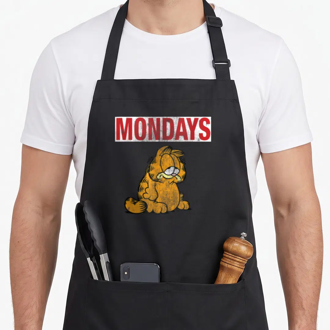 Monday cat apron - Red MONDAYS text above grumpy orange cat in distressed style — shown on a black cotton canvas apron against a white background