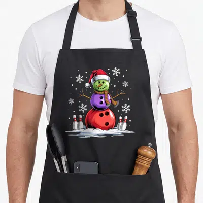 Bowling christmas snowman apron - Cartoon snowman made of red green and purple bowling balls with pins and snowflakes — shown on a black cotton canvas apron against a white background