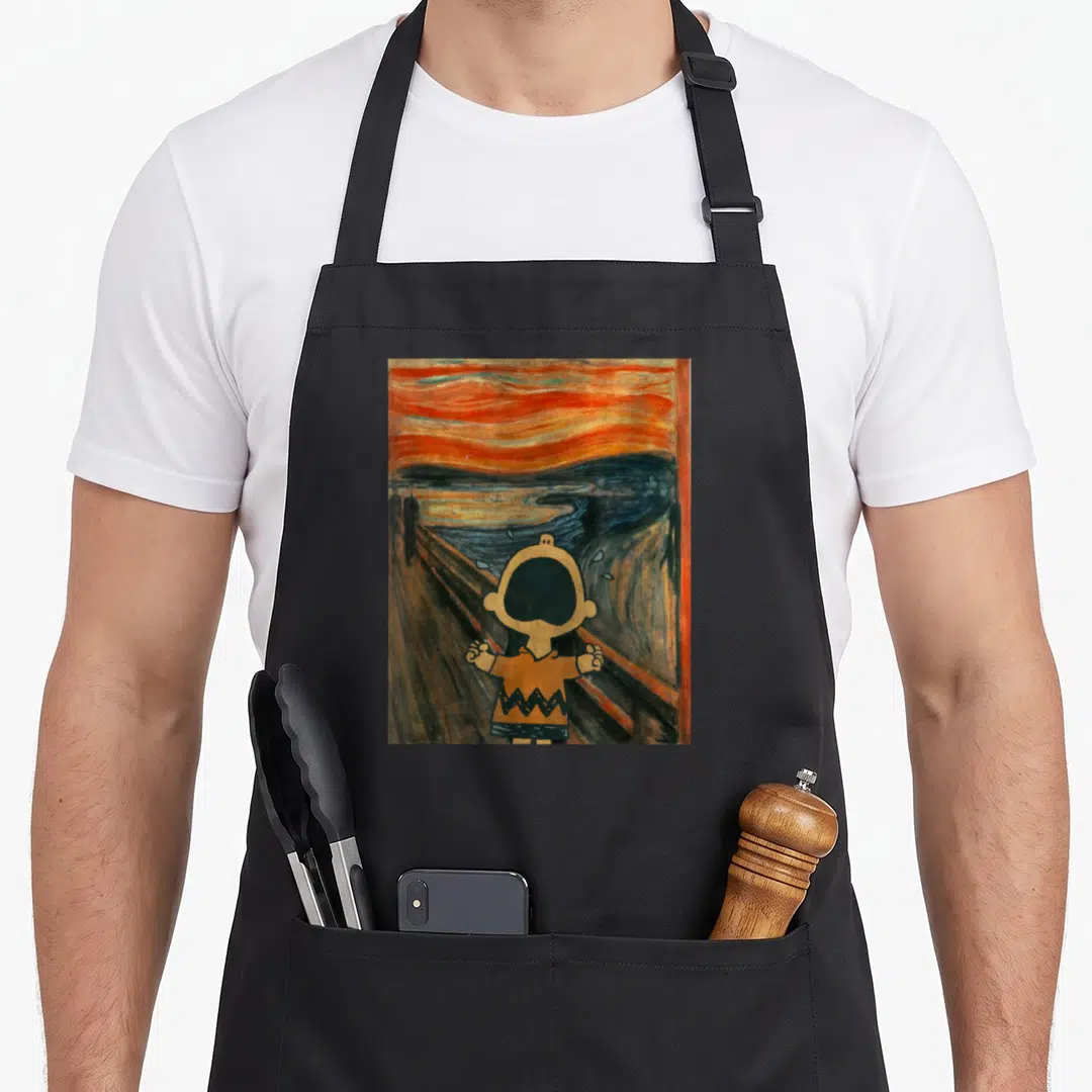 Charlie artsy aprons - Cartoon character screaming in front of orange sky and blue water bridge painting — shown on a black cotton canvas apron against a white background