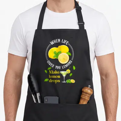 Give for love and lemons apron - Yellow lemons, green mint, cocktail glass, and white arched text on black fabric — shown on a black cotton canvas apron against a white background