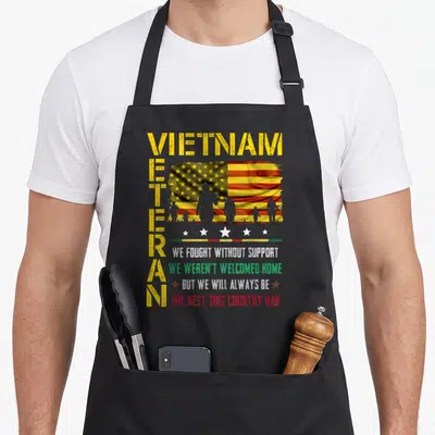 Fought veterans apron - Distressed yellow VIETNAM VETERAN text with multi-colored flag and soldier silhouettes — shown on a black cotton canvas apron against a white background