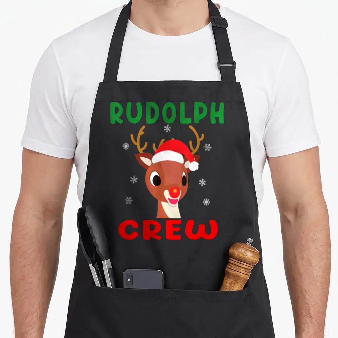 Rudolph family christmas aprons - Cartoon reindeer head in santa hat with RUDOLPH CREW text and six white snowflakes — shown on a black cotton canvas apron against a white background