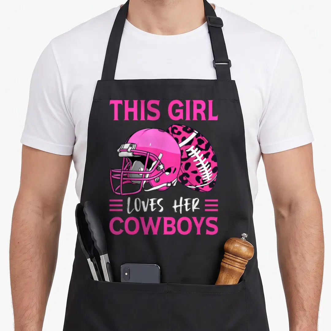 Cowboy football apron - Pink helmet and leopard print football with bold text reading THIS GIRL LOVES HER COWBOYS — shown on a black cotton canvas apron against a white background