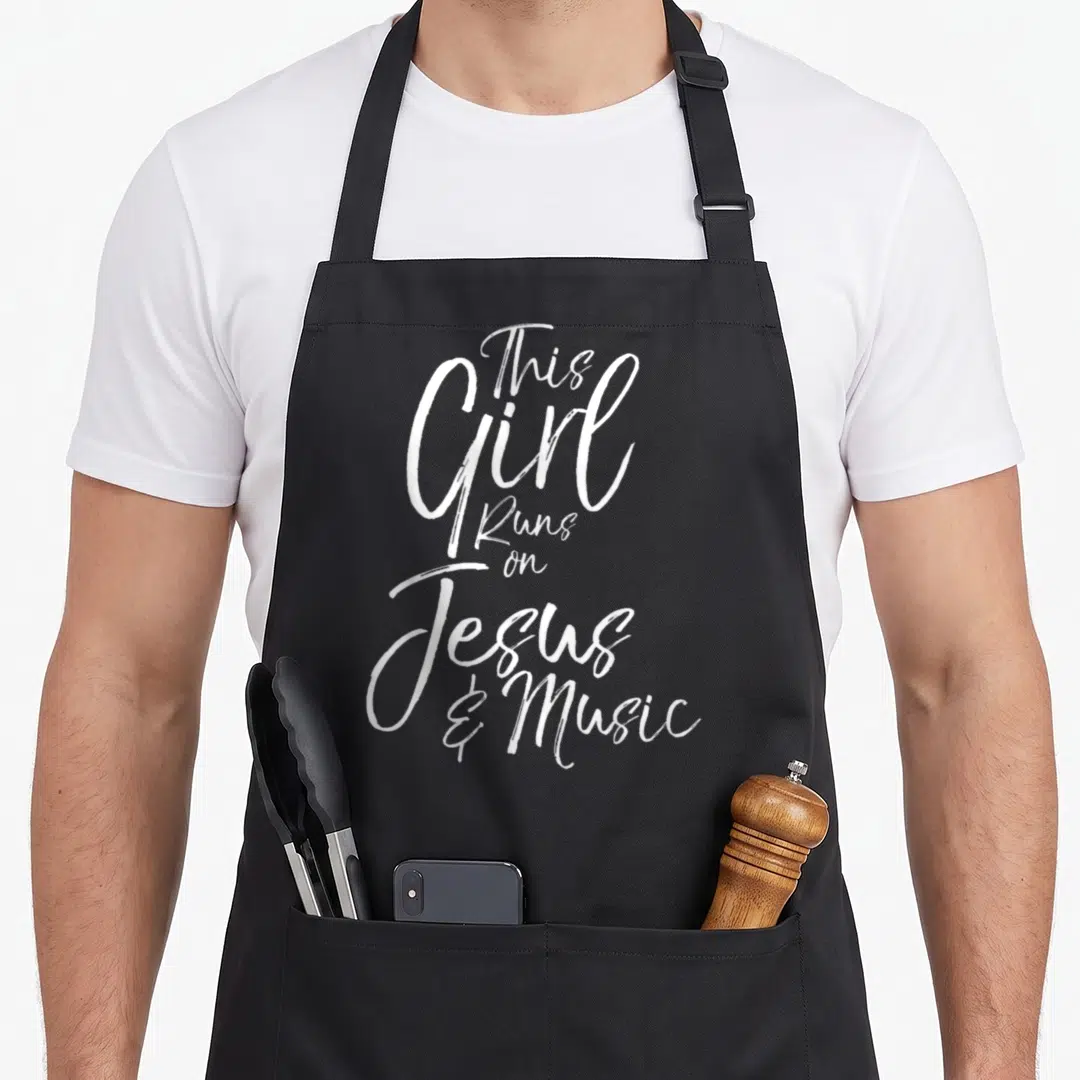 Musician christian apron - White stacked script text reading This Girl Runs on Jesus and Music — shown on a black cotton canvas apron against a white background