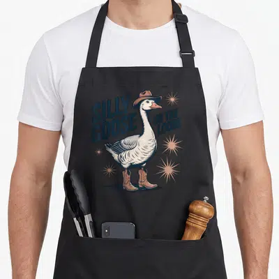 Vintage goose silly apron - Cartoon goose wearing brown hat and boots with blue text and tan starbursts — shown on a black cotton canvas apron against a white background
