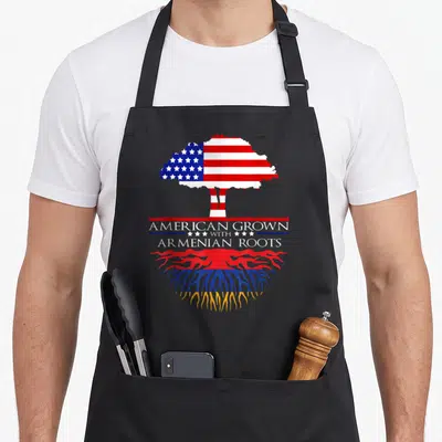 Armenian root american flag apron - Tree with US flag canopy and Armenian flag roots and stacked text — shown on a black cotton canvas apron against a white background
