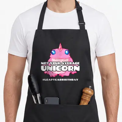 Leap unicorn birthday apron - Pink frog with unicorn horn and Not Your Average Unicorn text — shown on a black cotton canvas apron against a white background
