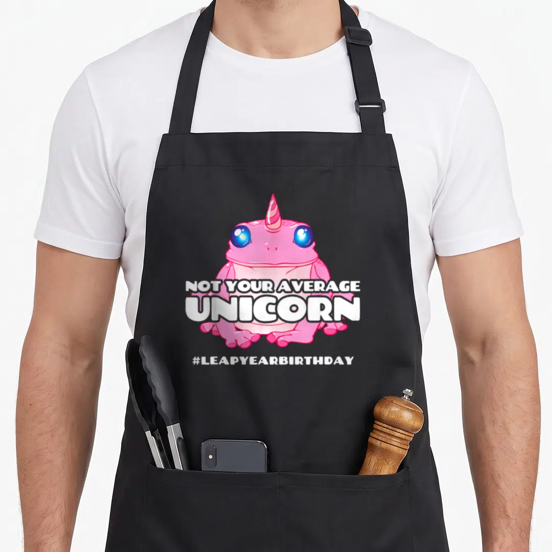 Leap unicorn birthday apron - Pink frog with unicorn horn and Not Your Average Unicorn text — shown on a black cotton canvas apron against a white background