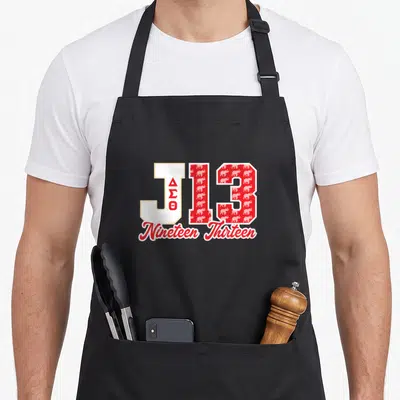 Theta january sorority apron - J13 typography with stacked Greek letters and red elephant pattern filling the numbers — shown on a black cotton canvas apron against a white background