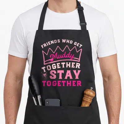 Run friends apron - Pink crown outline with 'Muddy Together Stay Together' distressed text and mud splatter graphic — shown on a black cotton canvas apron against a white background