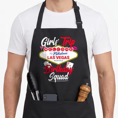 Las birthday apron - Las Vegas sign graphic with Girls Trip Birthday Squad text, dice, cards, cocktail, and lips — shown on a black cotton canvas apron against a white background