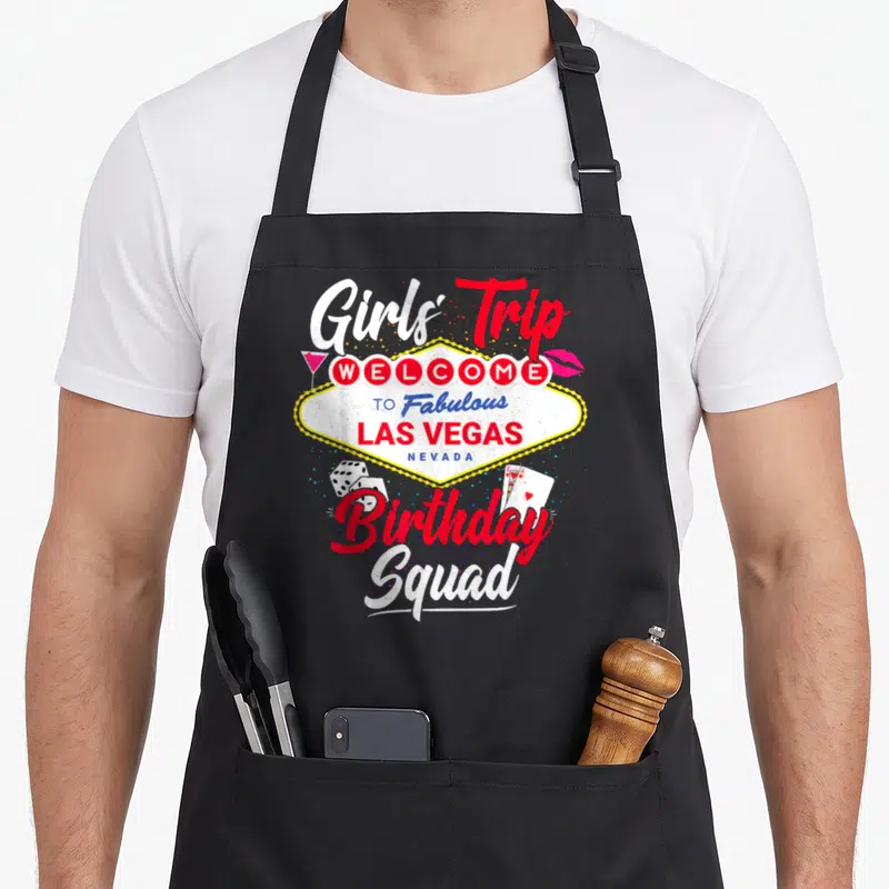 Las birthday apron - Las Vegas sign graphic with Girls Trip Birthday Squad text, dice, cards, cocktail, and lips — shown on a black cotton canvas apron against a white background